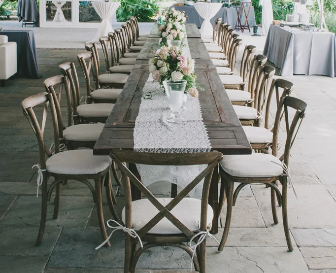 Bruiloftsstoelen in natuurlijke stijl met gekruiste stoelen op het terras, compleet met eettafel en bloemendecoraties